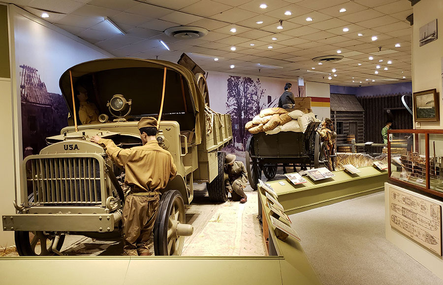 A museum exhibit inside the US Army Transportation Museum including a US Army truck and a wagon.